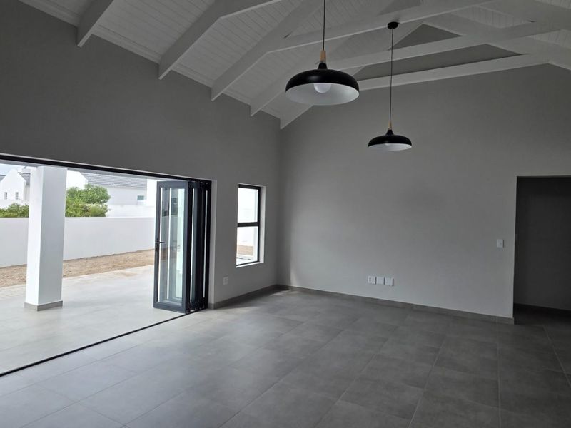 Spacious living area featuring a vaulted ceiling with exposed rafters, large bi-fold doors opening to a patio, and modern tiled flooring.