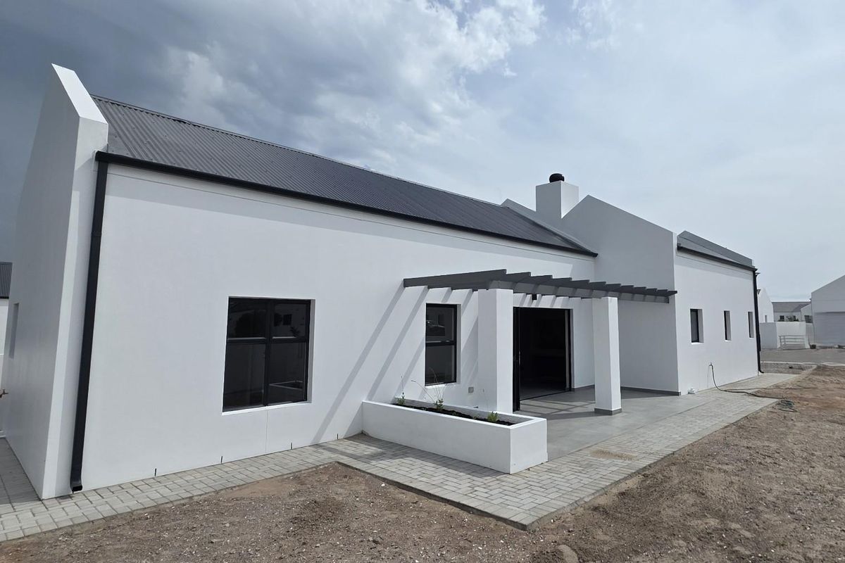 Modern rear exterior view featuring a white facade, corrugated metal roof, paved patio area with a pergola, and a built-in planter box.