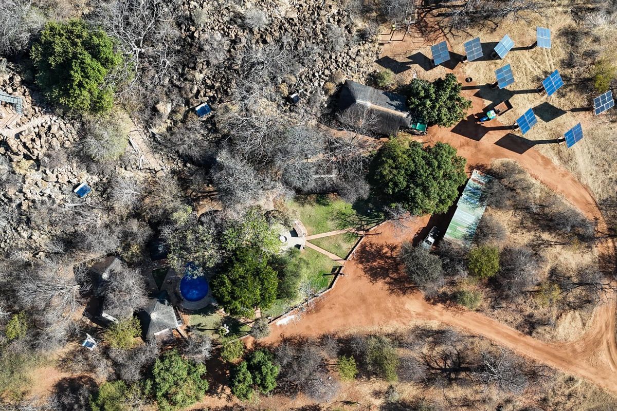 Aerial view of a rural farm property featuring multiple thatched roof buildings, a swimming pool, and a ground-mounted solar panel array.