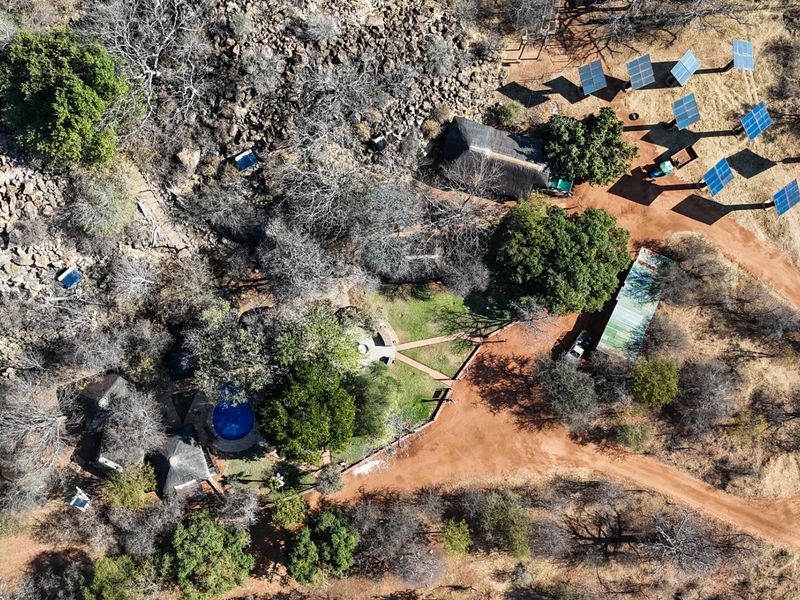 Aerial view of a rural farm property featuring multiple thatched roof buildings, a swimming pool, and a ground-mounted solar panel array.