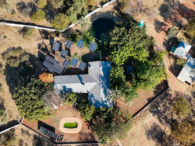 Aerial view of a farm property featuring a main residence with a metal roof, solar panel array, swimming pool, and water reservoir.