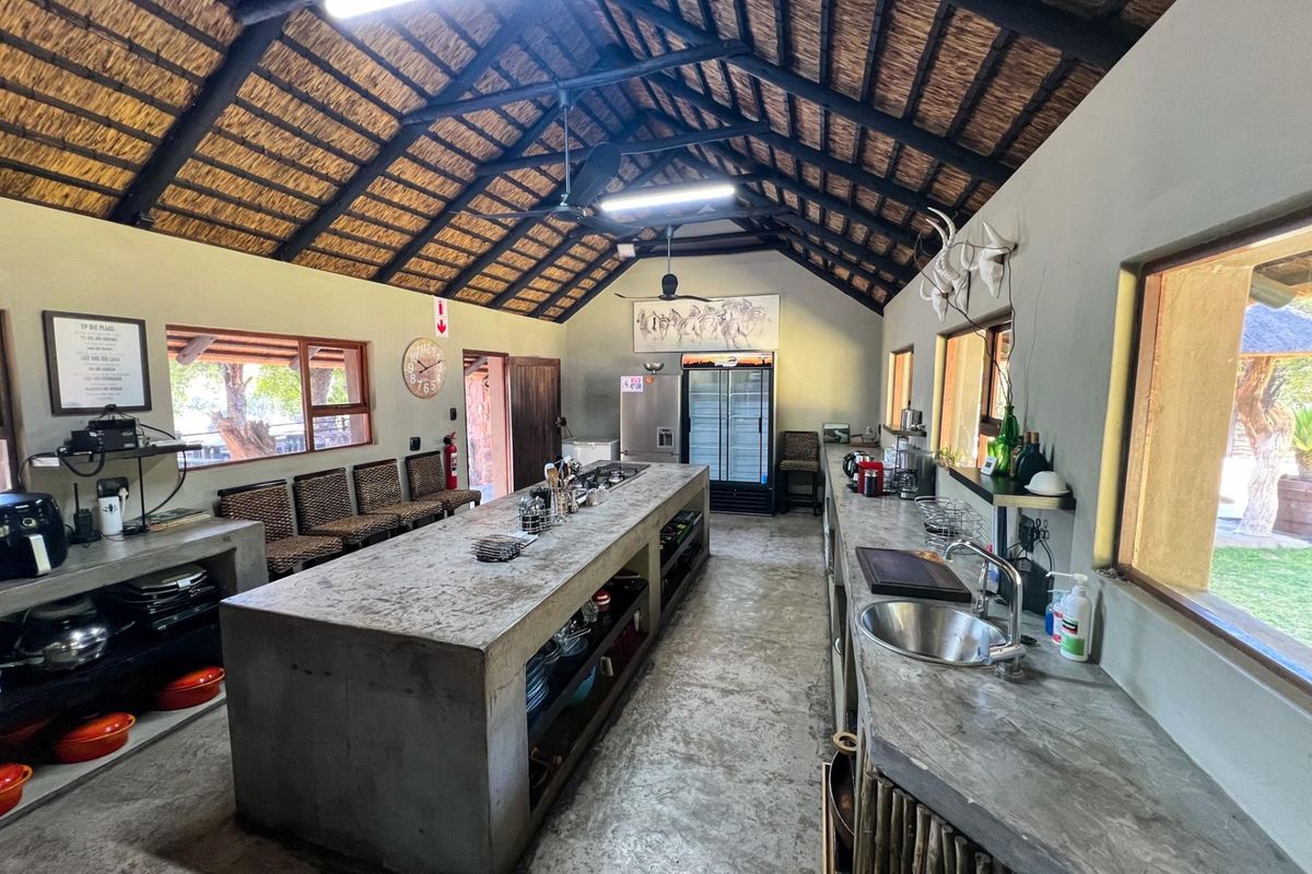 Spacious rustic kitchen featuring a large concrete island, concrete countertops, exposed thatch roofing with timber trusses, and ample built-in storage.