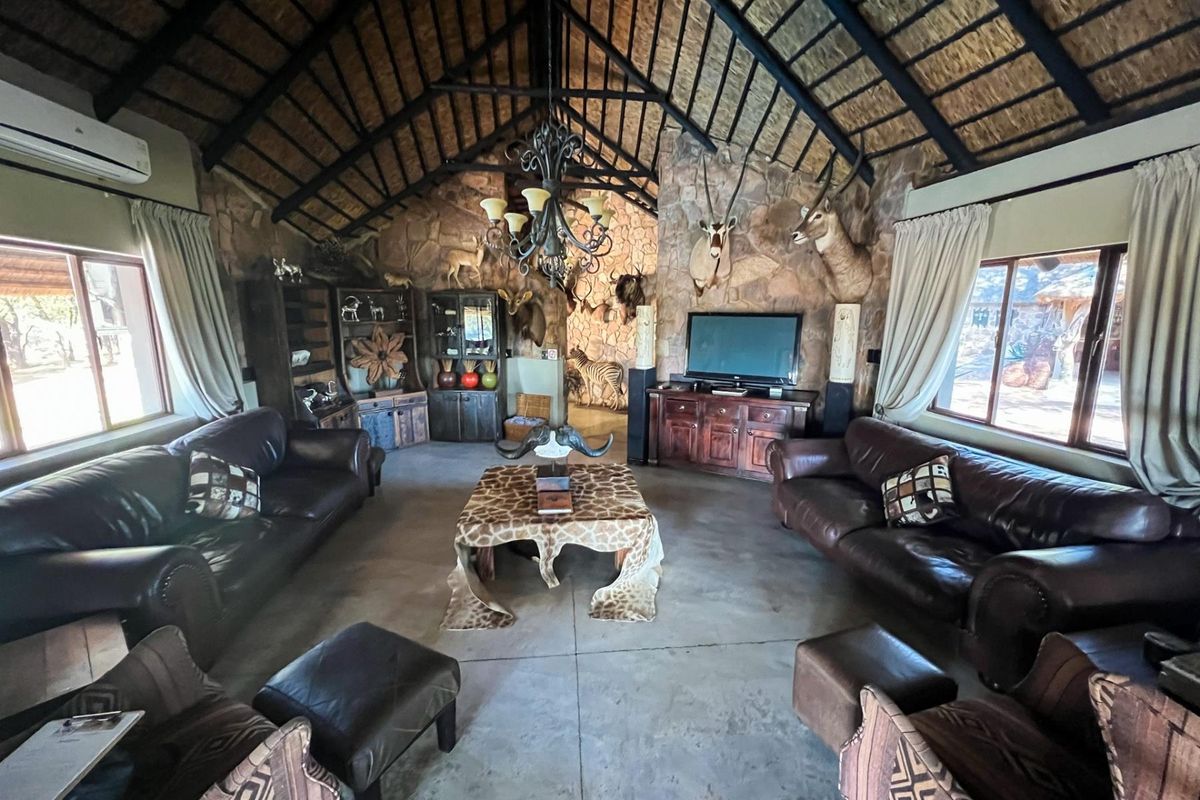 Spacious living room featuring a high vaulted thatched ceiling with exposed timber trusses, stone feature walls, and polished concrete flooring.