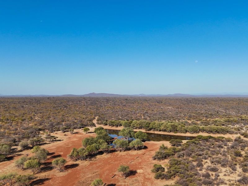 An aerial view of the expansive farm landscape featuring a natural water dam surrounded by native trees and open bushveld terrain.
