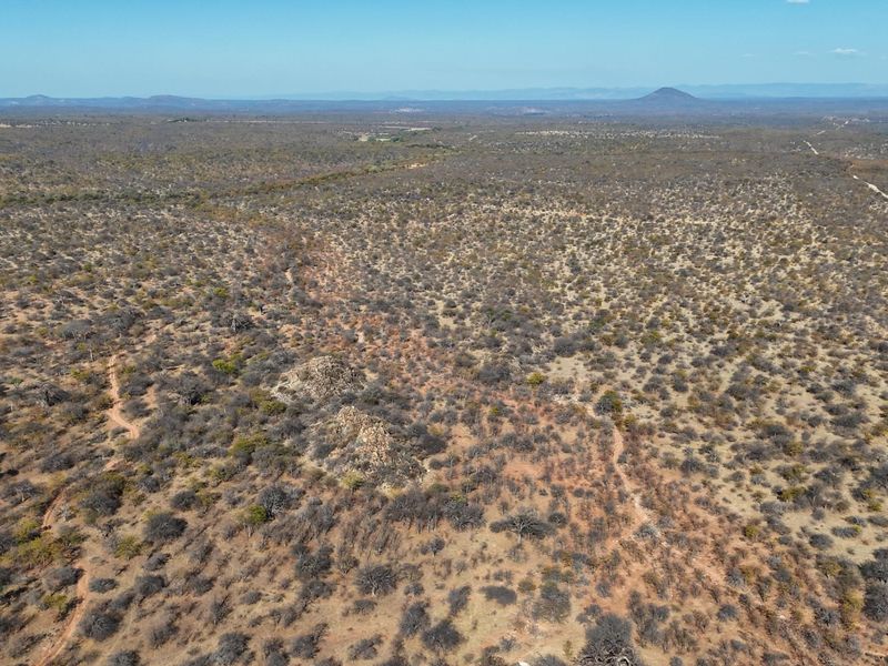 An expansive aerial view of the vast, natural farm landscape featuring rugged terrain and native vegetation under a clear sky.