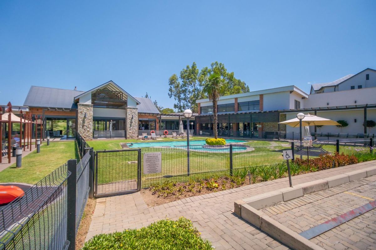 A well-maintained communal pool area featuring a landscaped garden, stone-clad building architecture, and paved walkways within a secure residential complex.