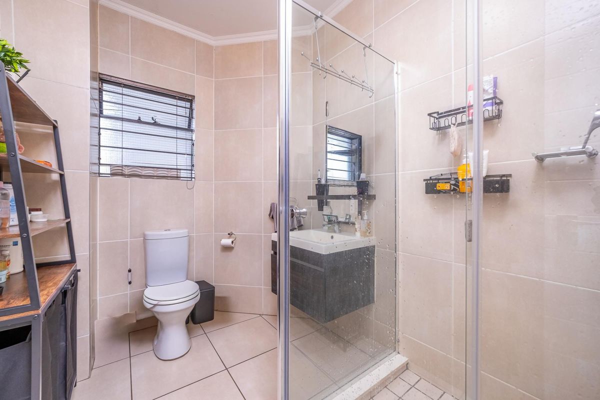 A functional bathroom featuring a glass-enclosed shower, a modern vanity cabinet with a washbasin, and neutral floor-to-ceiling wall tiles.