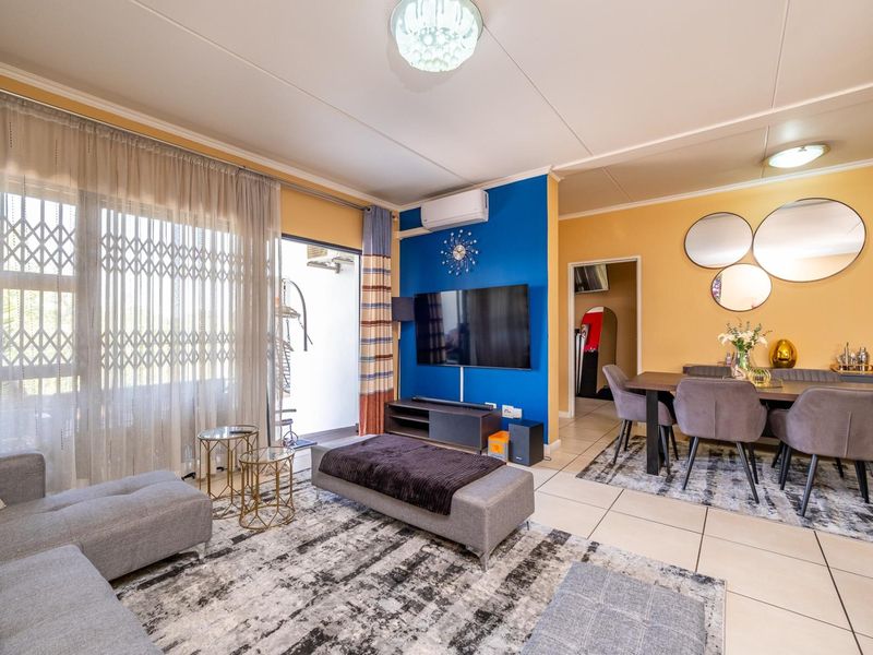 Open-plan living and dining area featuring tiled flooring, a split-system air conditioner, and direct access to a balcony through a sliding glass door.