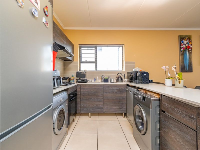 Compact kitchen featuring dark wood-look cabinetry, tiled flooring, integrated appliances, and a breakfast bar counter.