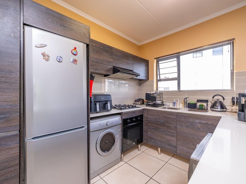 Compact kitchen featuring modern wood-grain cabinetry, gas hob, built-in oven, extractor fan, and tiled finishes with a functional layout.