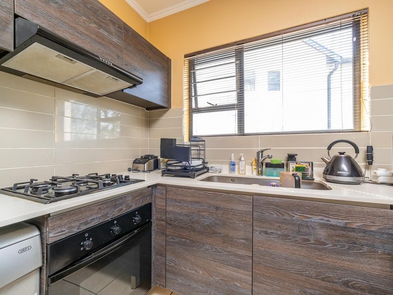 Compact kitchen featuring wood-look cabinetry, gas hob, built-in oven, extractor fan, and a stainless steel sink with tiled backsplash.