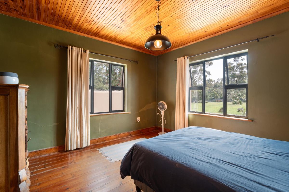 A bedroom featuring timber ceiling and flooring, aluminium window frames, and green painted walls with visible plaster cracking.