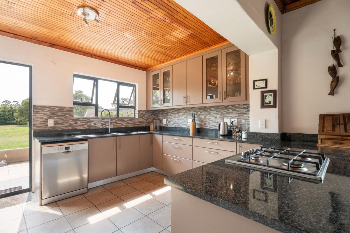 A well-maintained kitchen featuring granite countertops, a built-in gas hob, mosaic backsplash, and a warm timber ceiling with direct access to the garden.