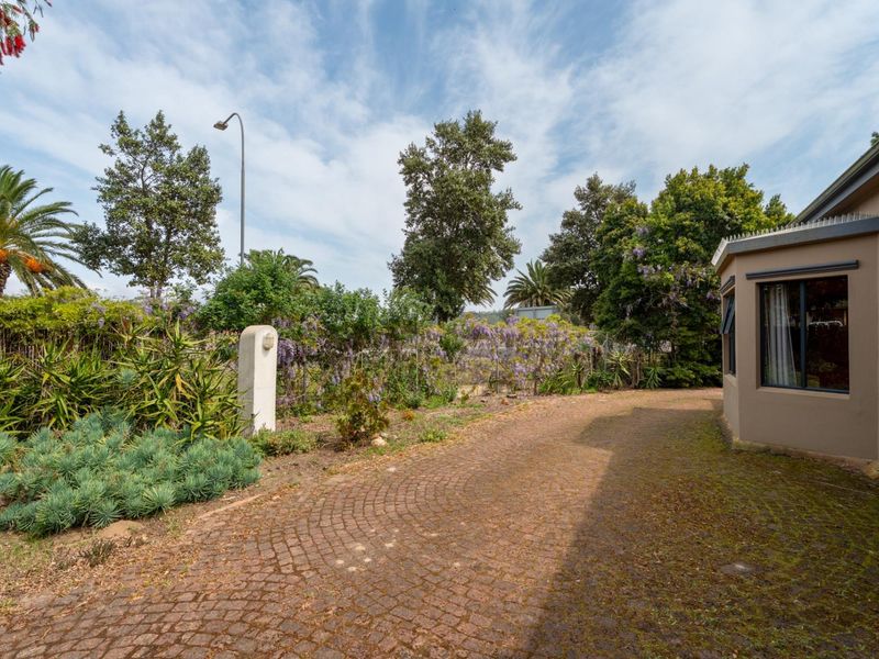 A view of the property's front exterior featuring a cobblestone driveway, established garden landscaping, and exterior building facade.