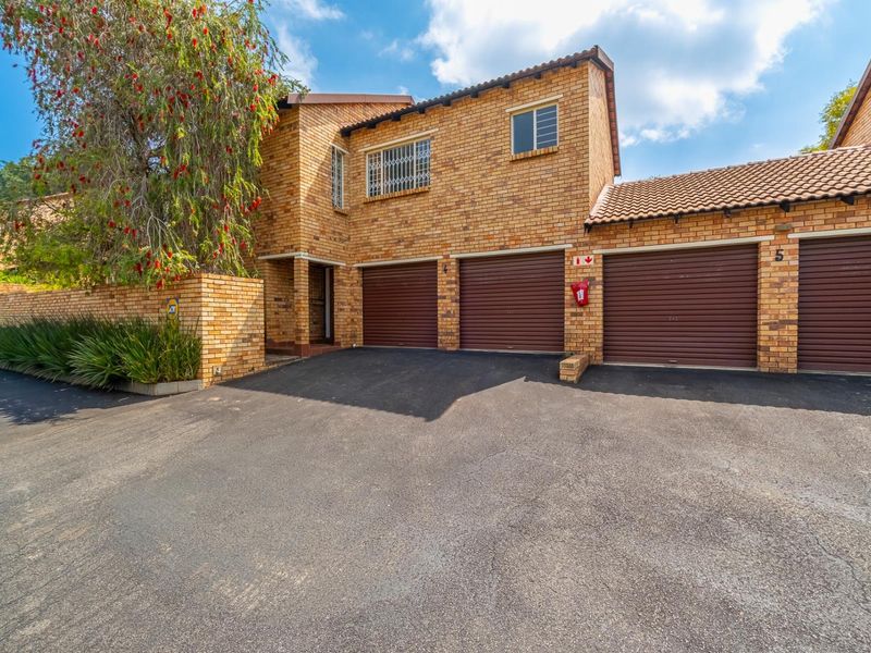 Front elevation of a face brick townhouse featuring three roller shutter garage doors and an asphalt driveway.