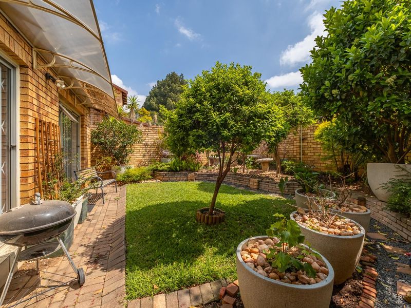 A well-maintained private garden featuring a brick-paved patio area, raised garden beds, and a lush lawn enclosed by brick boundary walls.