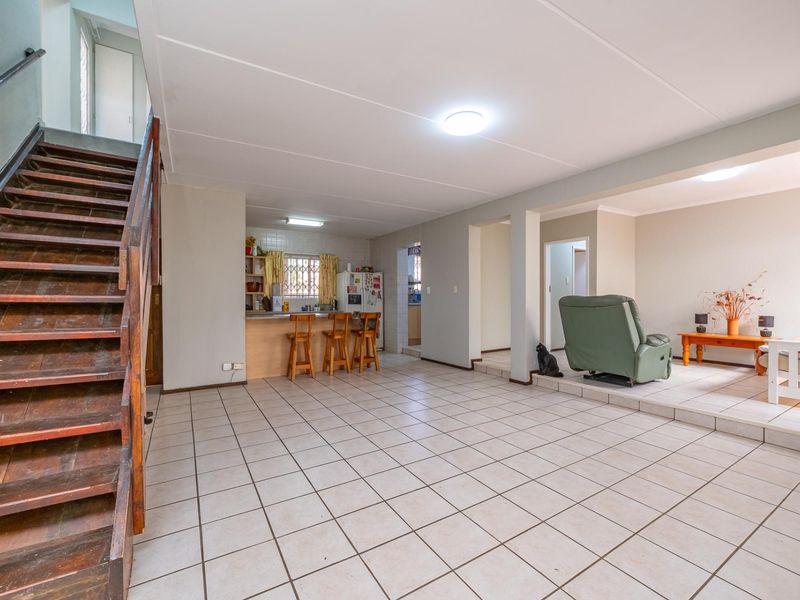Open-plan living area featuring tiled floors, a wooden staircase, and a functional kitchen with a breakfast counter.