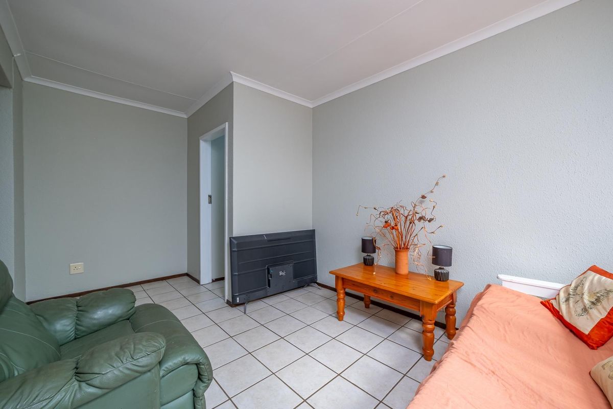 A living room area featuring neutral wall paint, tiled flooring, and coved ceiling details, providing a functional and versatile space.