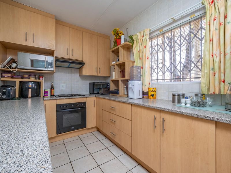 Functional kitchen featuring light wood-finish cabinetry, granite-look laminate countertops, built-in oven, electric hob, and tiled flooring with a window security gate.