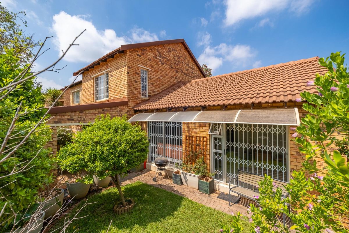 Rear view of a brick townhouse featuring a paved patio area, security gates, and a well-maintained garden.