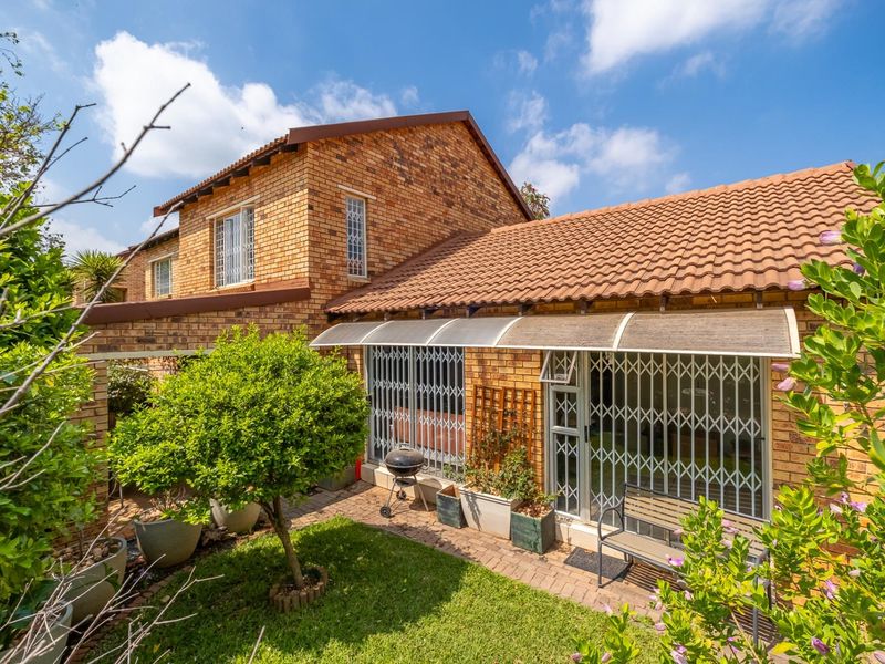 Rear view of a brick townhouse featuring a paved patio area, security gates, and a well-maintained garden.