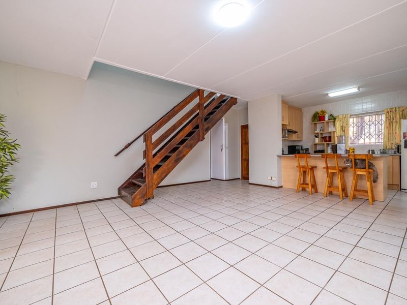 Open plan living area featuring tiled flooring, a wooden staircase, and a functional kitchen with a breakfast bar counter.