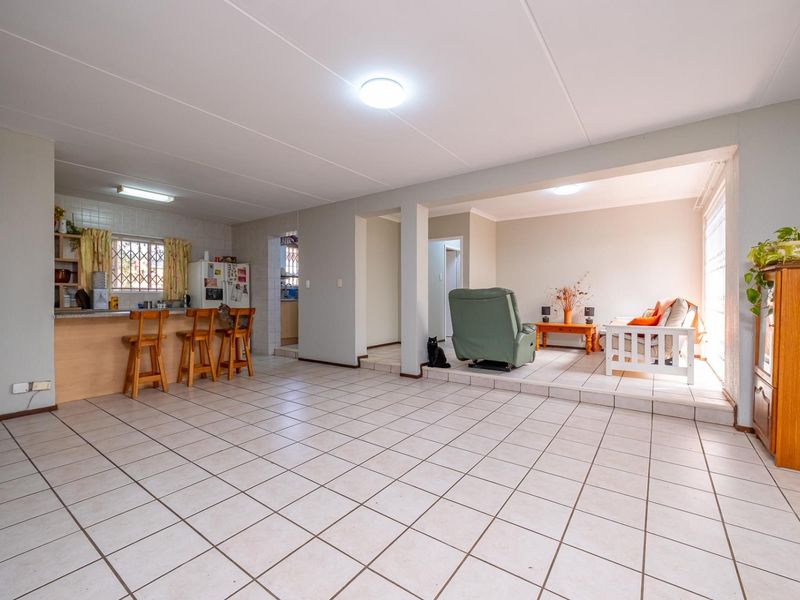 Spacious open-plan living area featuring a tiled floor, a kitchen with a breakfast bar, and a sunken lounge space with natural light.