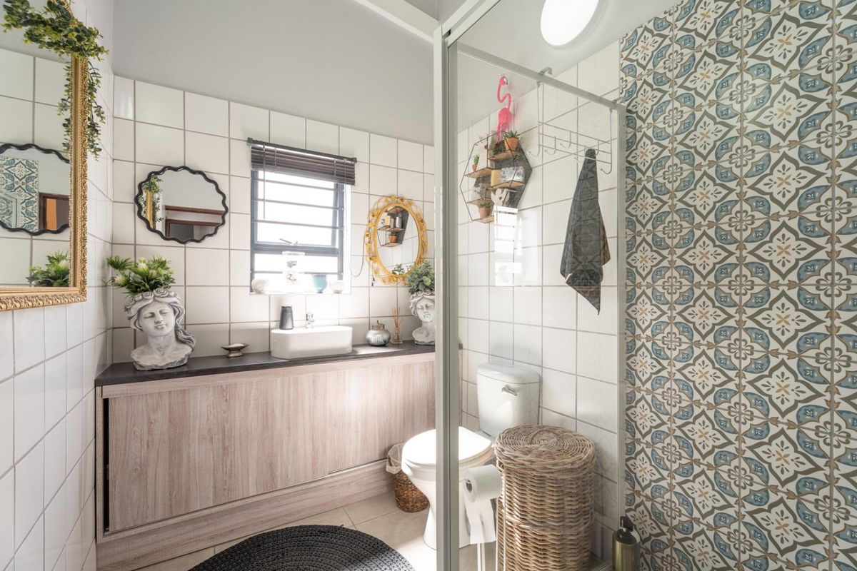 A well-maintained bathroom featuring a vanity cabinet with a countertop basin, a toilet, and a shower enclosure with decorative patterned wall tiles.