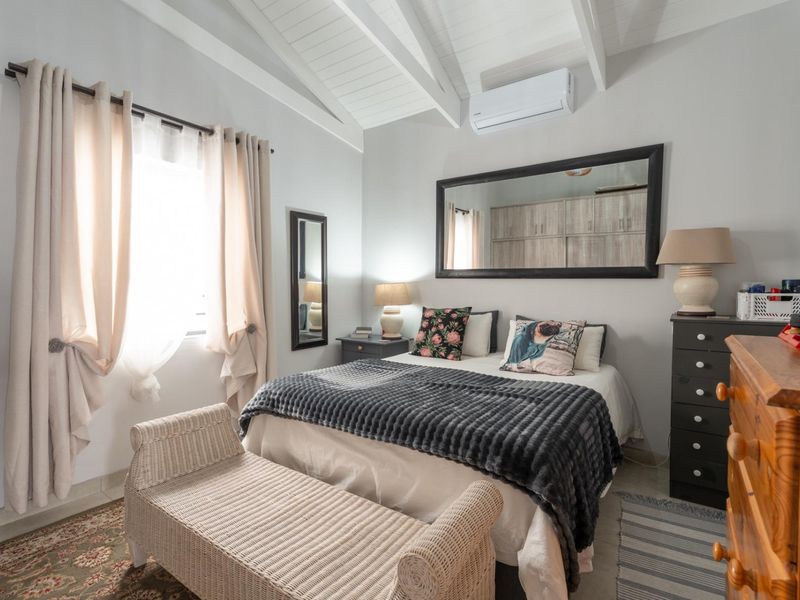 A well-maintained bedroom featuring a vaulted ceiling with exposed rafters, tiled flooring, and a wall-mounted air conditioning unit.