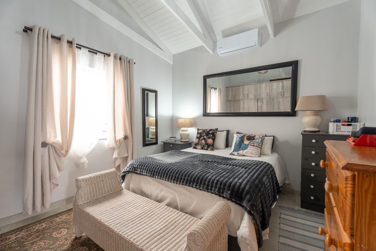 A well-maintained bedroom featuring a vaulted ceiling with exposed rafters, tiled flooring, and a wall-mounted air conditioning unit.
