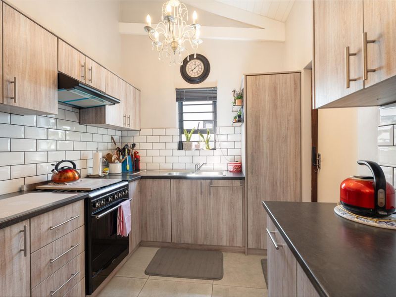 A well-maintained kitchen featuring light wood-grain cabinetry, subway tile backsplash, dark countertops, and a vaulted ceiling with a decorative chandelier.