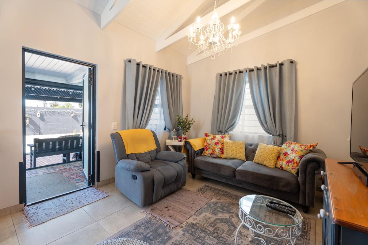 A bright living room featuring a vaulted ceiling with exposed beams, a decorative chandelier, tiled flooring, and direct access to an outdoor patio area.