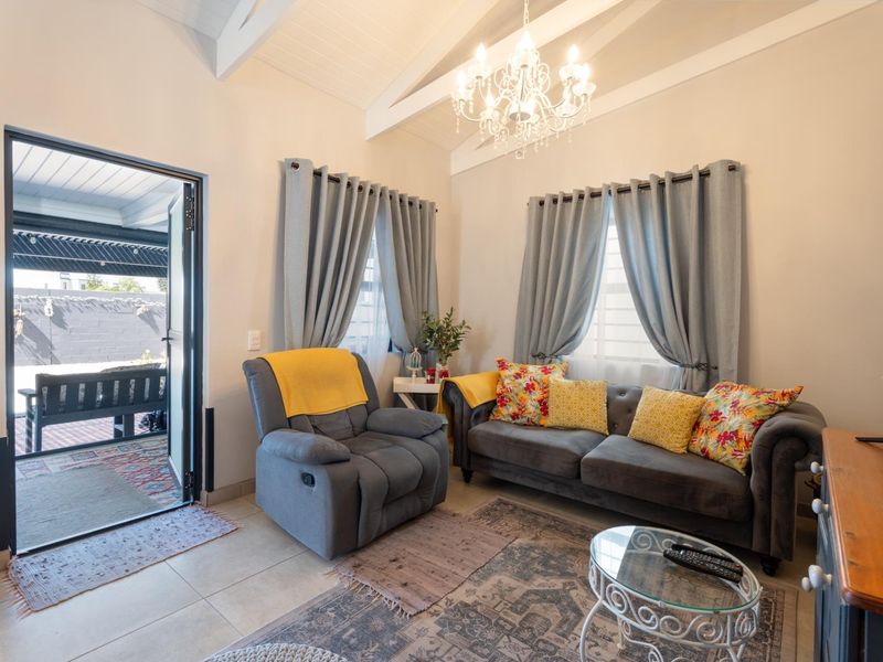 A bright living room featuring a vaulted ceiling with exposed beams, a decorative chandelier, tiled flooring, and direct access to an outdoor patio area.