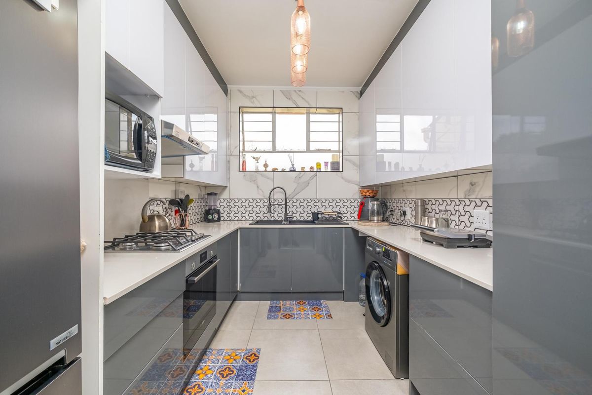 Modern galley kitchen featuring high-gloss cabinetry, quartz countertops, integrated appliances, gas hob, and stylish marble-look wall tiling.