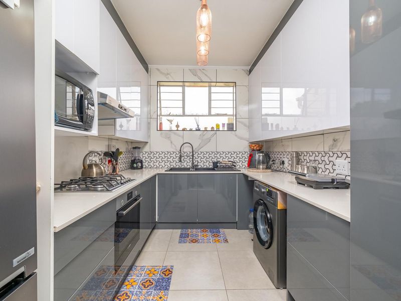 Modern galley kitchen featuring high-gloss cabinetry, quartz countertops, integrated appliances, gas hob, and stylish marble-look wall tiling.