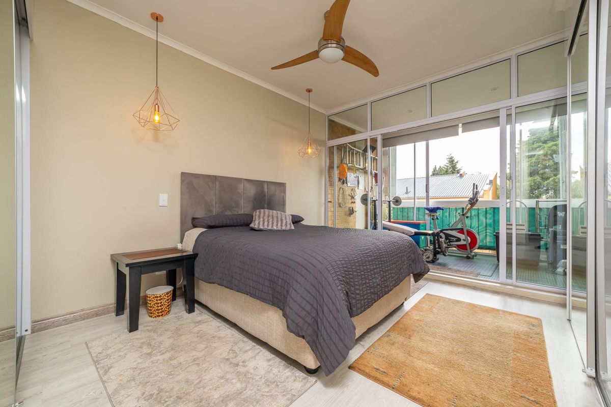 A well-lit bedroom featuring laminate flooring, a ceiling fan, and large sliding glass doors that provide access to an adjacent balcony.