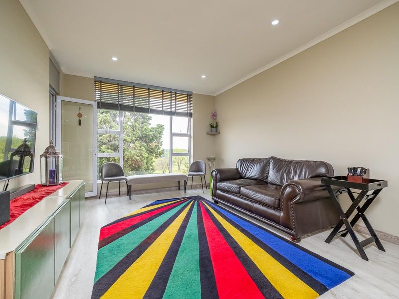 A bright living room featuring laminate flooring, recessed downlights, and large windows providing natural light and access to an outdoor area.