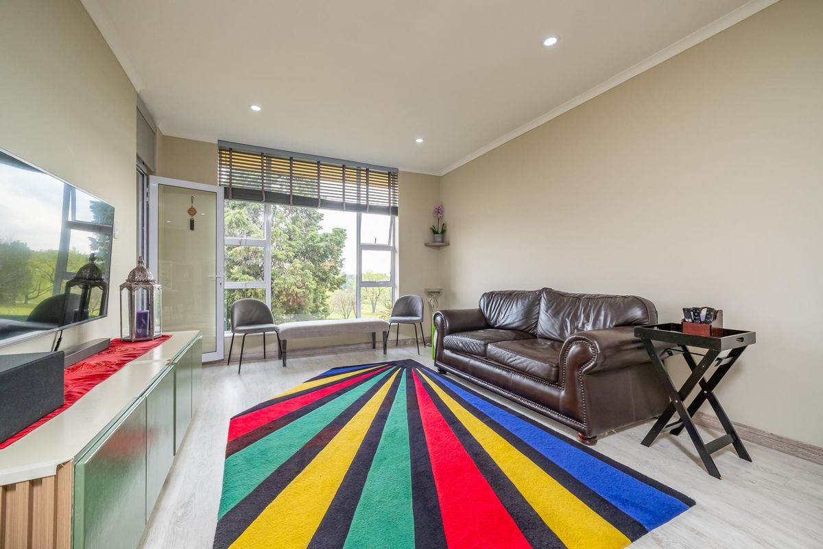 A bright living room featuring laminate flooring, recessed downlights, and large windows providing natural light and access to an outdoor area.