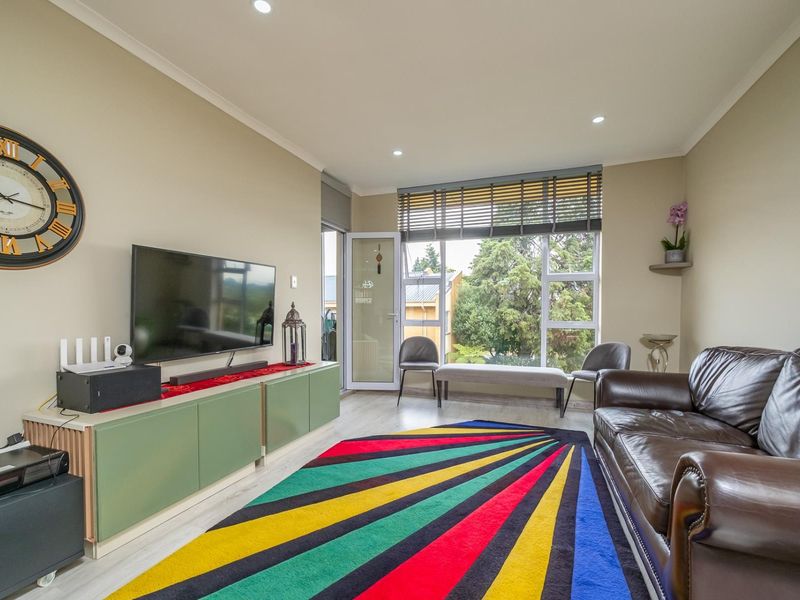 A bright living room featuring laminate flooring, recessed downlights, and a large window with access to an outdoor area.