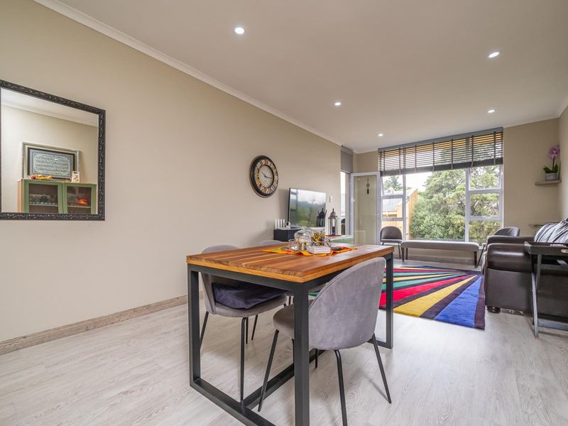 A bright open-plan living and dining area featuring modern laminate flooring, recessed downlighting, and large windows providing natural light and outdoor access.
