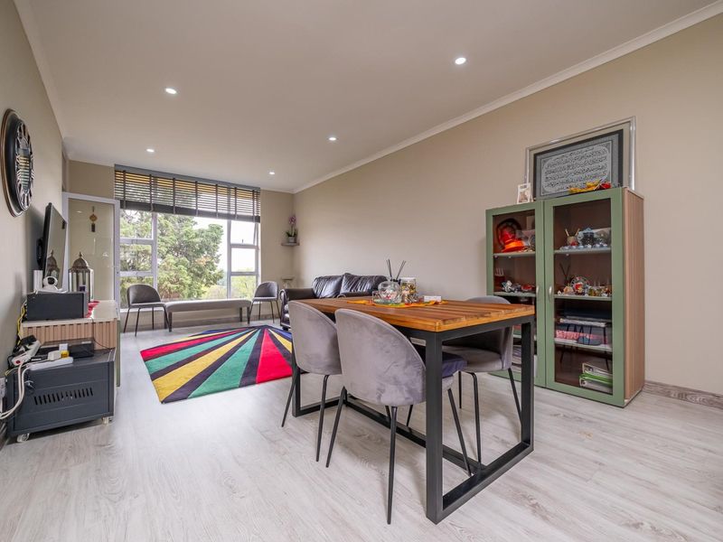 A bright open-plan living and dining area featuring modern laminate flooring, recessed downlighting, and large windows providing natural light.