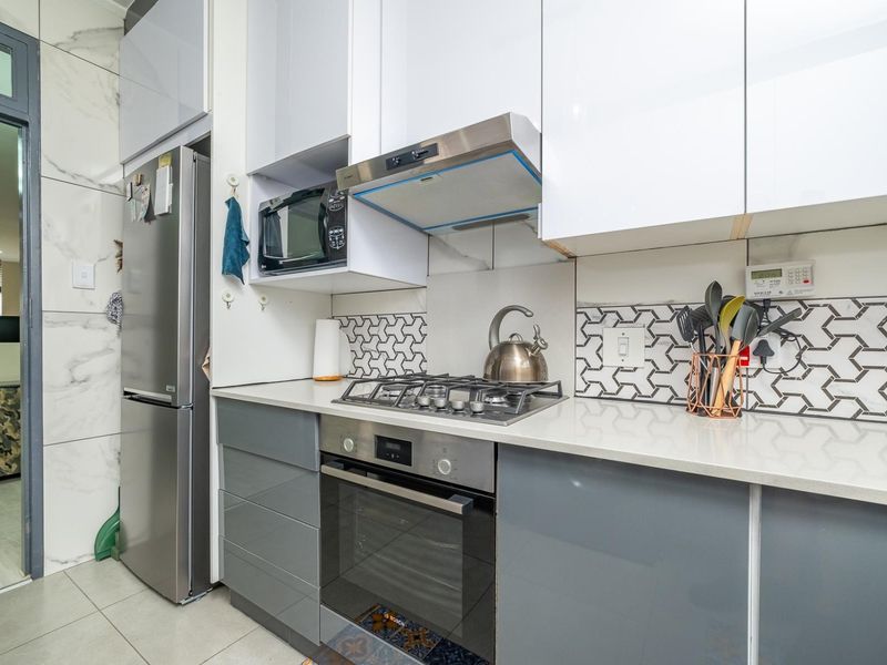 Modern kitchen featuring high-gloss cabinetry, quartz countertops, a gas hob, built-in oven, and a stylish geometric tiled backsplash.