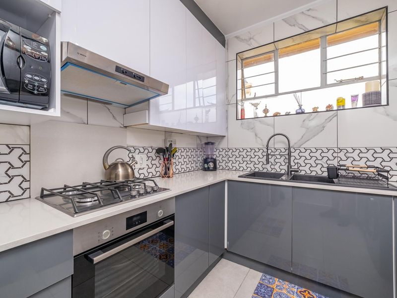 Modern kitchen featuring high-gloss cabinetry, quartz countertops, gas hob, built-in oven, extractor fan, and stylish geometric tiled backsplash with a double sink.