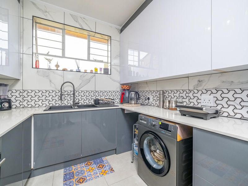 Modern kitchen featuring high-gloss grey cabinetry, white quartz countertops, marble-effect wall tiles, and integrated appliances including a built-in oven and washing machine.
