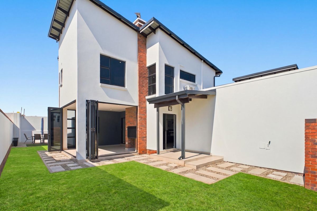 Rear view of a modern two-story house featuring a covered patio, bi-fold doors, brick accents, and a well-maintained garden.