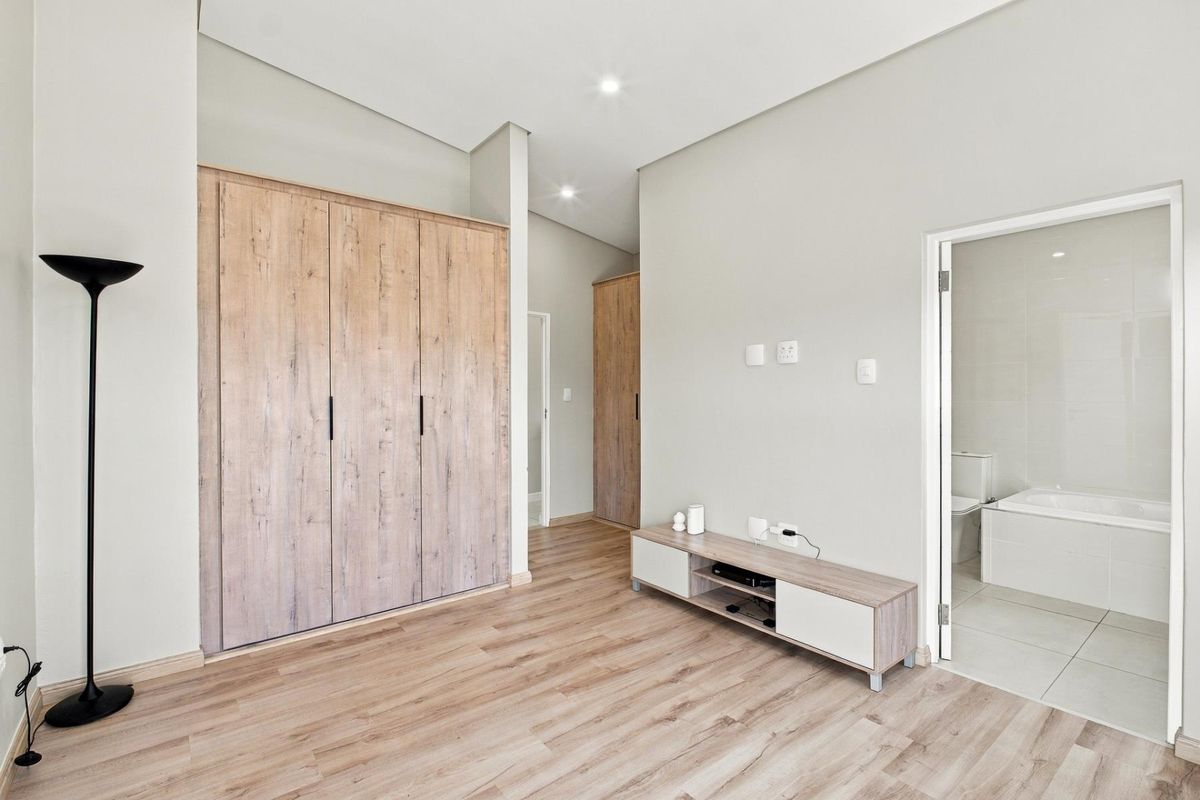 Modern bedroom featuring light wood-look laminate flooring, ample built-in cupboard space, and direct access to an en-suite bathroom.