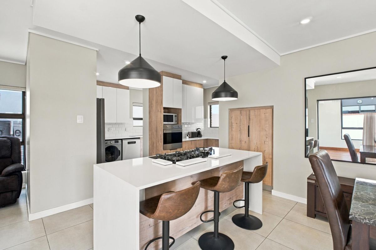 Modern kitchen featuring a central island with a gas hob, sleek white and wood-tone cabinetry, built-in appliances, and contemporary pendant lighting.