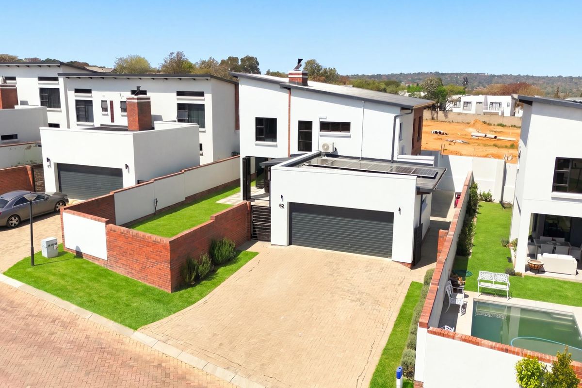 Aerial view of a modern two-story house featuring a paved driveway, double garage, solar panels, and well-maintained garden areas within a residential estate.