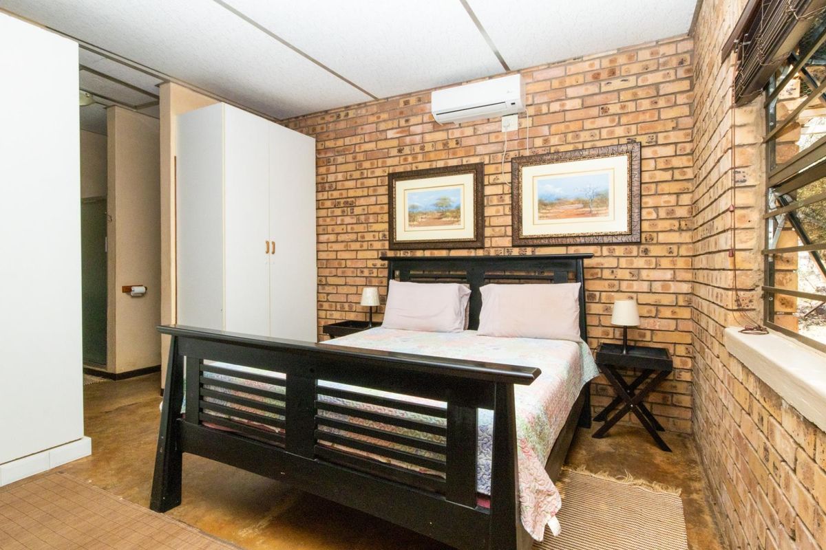 A bedroom featuring exposed brick walls, a split-system air conditioner, and built-in storage, offering a rustic aesthetic with potential for modern updates.