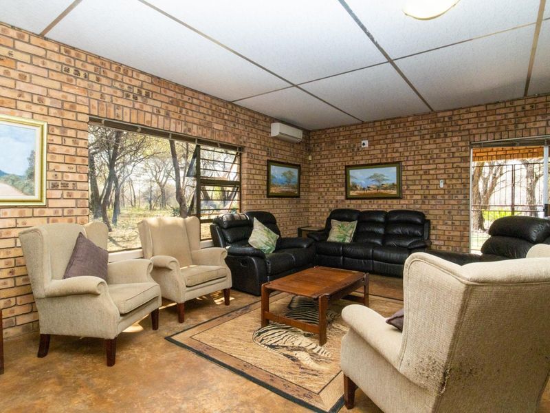 A rustic living room featuring exposed brick walls, concrete flooring, and large windows that provide natural light and views of the surrounding farm landscape.